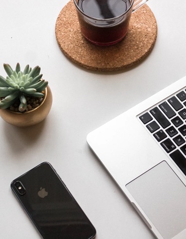 A desk with a cactus, tea, cellphone, and laptop.